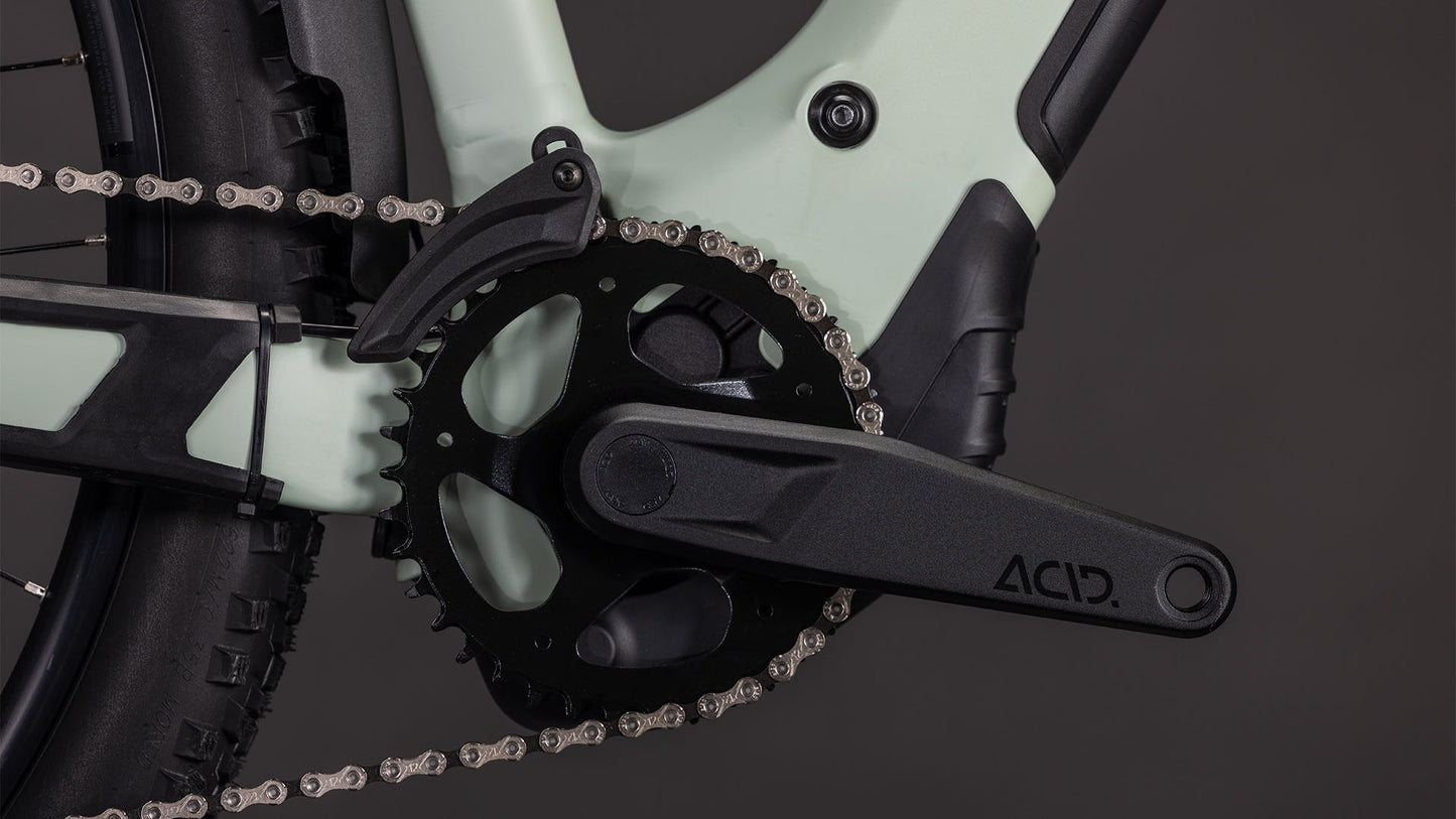 Nahaufnahme des CUBE Reaction Hybrid Pro 800 FE Trapeze 2026 in desertstone'n'driedherbs mit schwarzer ACID-Kurbelgarnitur, Kettenblatt und Kette. In den grün-schwarzen Rahmen sind ein Bosch CX Motor und eine Shimano XT 12-fach Schaltung integriert; der Hinterreifen ist teilweise zu sehen.