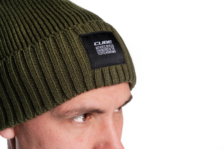 Nahaufnahme einer Person, die die Cube CUBE Beanie oliv mit schwarzem "CUBE"-Aufnäher trägt, mit Blick zur Seite vor weißem Hintergrund - ideal für kühle Tage in Niedersachsen.