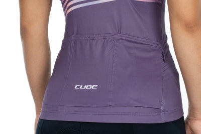 Jemand trägt das CUBE TEAMLINE WS Trikot kurzarm violet'n'sand, ein tailliertes, kurzärmeliges Radtrikot von Cube mit mehreren Rückentaschen und aus Funktionsmaterial. Der Markenname steht auf der Rückentasche.