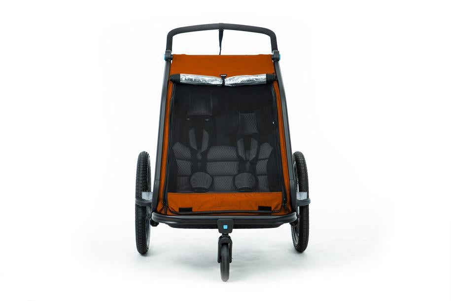 Frontansicht des Cube CUBE Kinder Fahrradanhänger Double CMPT X Actionteam in Orange, mit schwarzem Insektenschutznetz, zwei Sitzen und drei Rädern, dargestellt vor weißem Hintergrund.