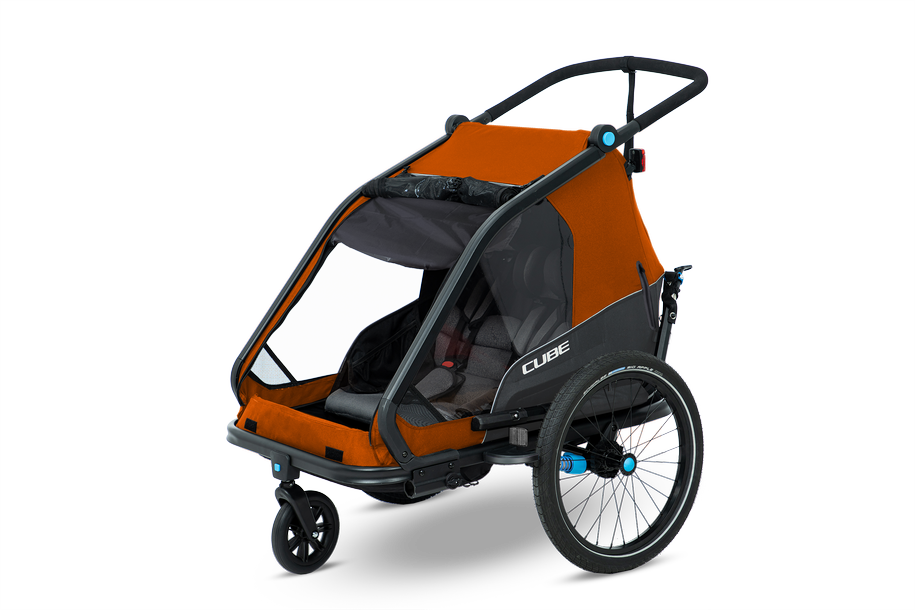 Der Cube CUBE Kinder Fahrradanhänger Double CMPT X Actionteam ist ein orange-schwarzer Kinderfahrradanhänger mit einem Insektenschutzgitter, zwei Sitzen, drei Rädern und einer hinteren Lenkstange, abgebildet auf einem schlichten weißen Hintergrund.