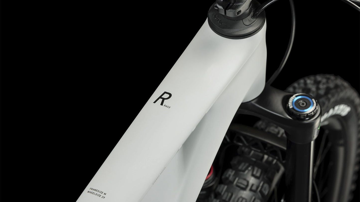 Nahaufnahme des CUBE Stereo ONE55 C:62 Race 29 lightgrey'n'grey 2024 Rahmens mit "R" und "Race" Schriftzug, der einen Teil des Lenkers, des Vorderreifens und der RockShox Lyrik Select+ Gabel vor einem schwarzen Hintergrund zeigt.