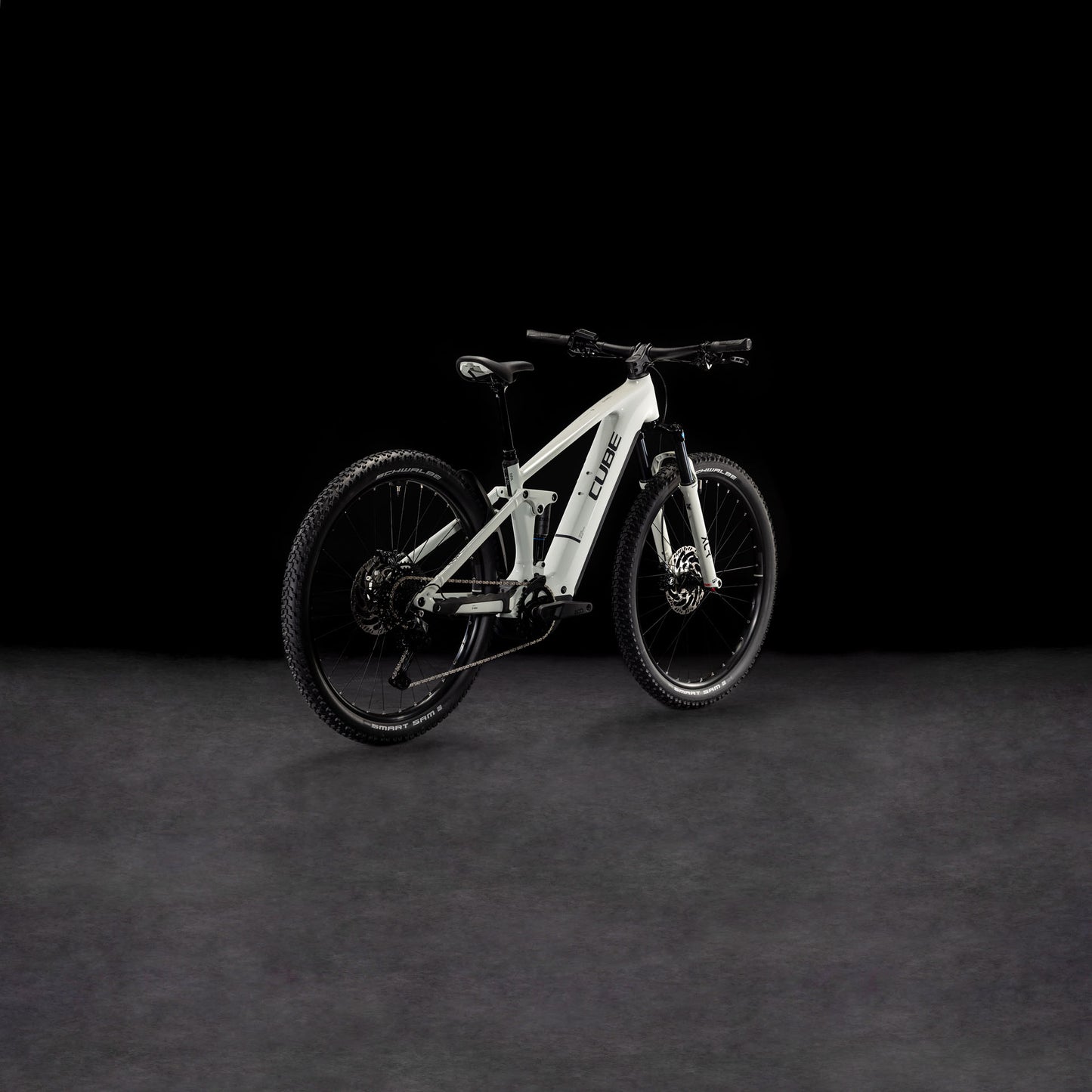 Das CUBE Stereo Hybrid ONE22 Pro 800 desertstone'n'black 2025 Elektro-Mountainbike mit schwarzen Laufrädern, Federung und Bosch CX Antrieb steht vor einem dunklen Hintergrund und ist nach links geneigt, um den Rahmen zu präsentieren.