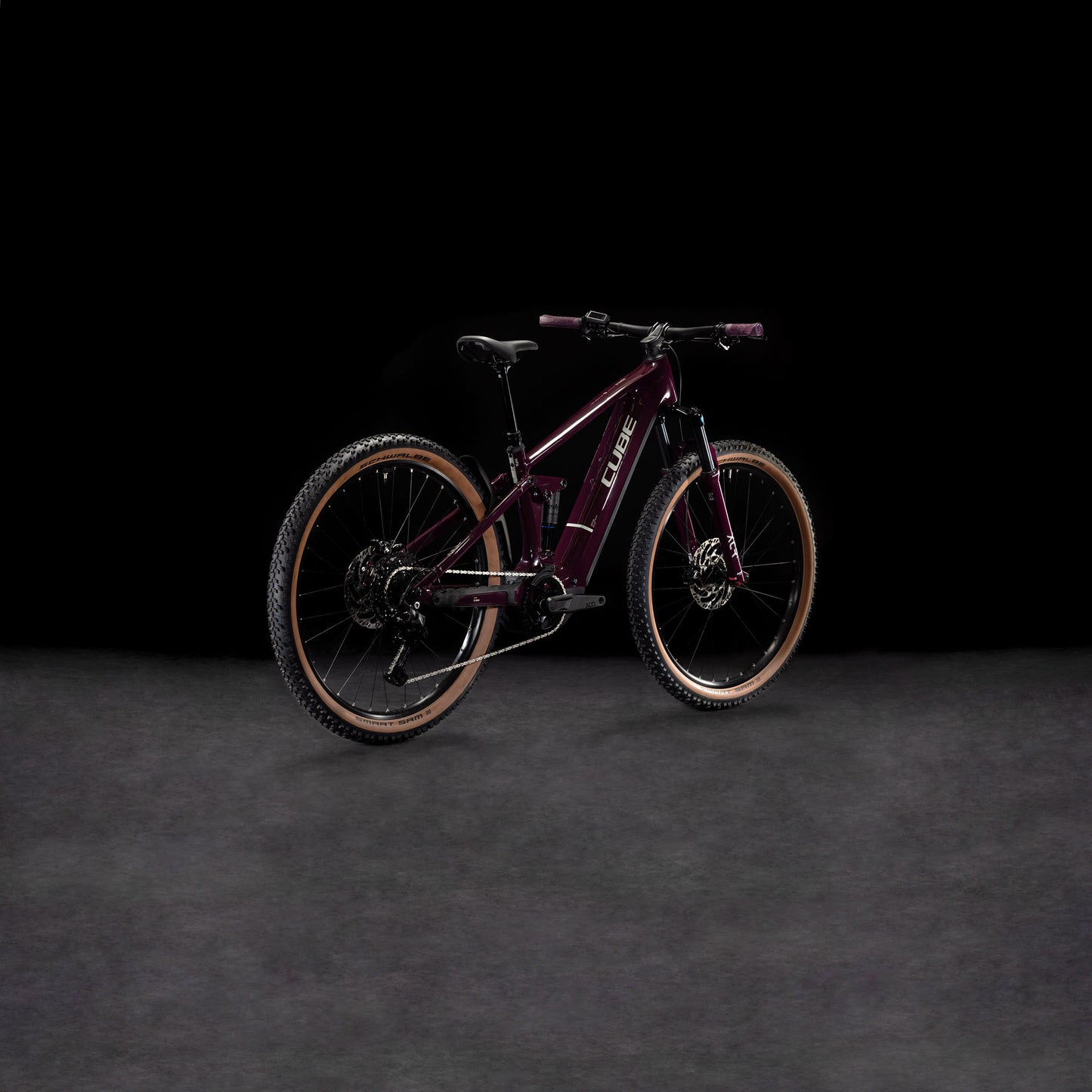 Das CUBE Stereo Hybrid ONE22 Pro 800 amarone'n'grey 2025 steht auf einer dunklen, strukturierten Oberfläche vor schwarzem Hintergrund, angewinkelt, um seinen Rahmen und Shimano Cues 10-fach Schaltung für präzise Schaltvorgänge zu präsentieren.