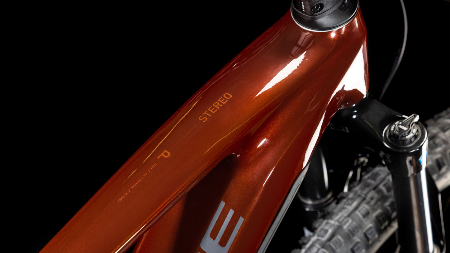 Nahaufnahme eines CUBE Stereo Hybrid ONE44 Pro 800 bourbon'n'black 2025 Rahmens mit der Aufschrift STEREO, wobei das Oberrohr, die Gabel und das Vorderrad vor einem schwarzen Hintergrund hervorgehoben werden.