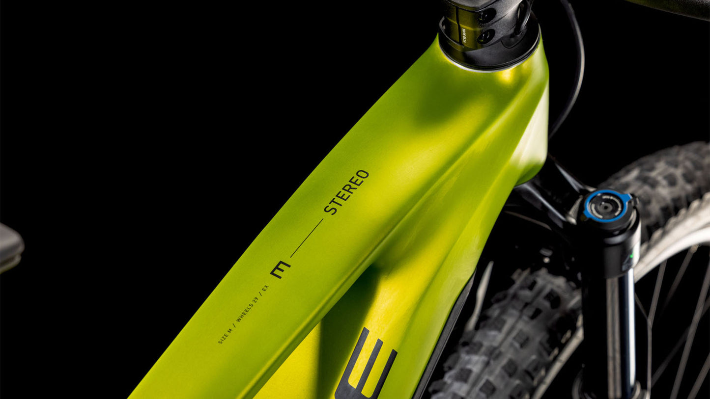 Nahaufnahme eines grünen CUBE Stereo Hybrid ONE44 EX 800 lizard'n'black 2025 Rahmens, der das Oberrohr mit dem Schriftzug "STEREO" sowie einen Teil der Federgabel und des Reifens vor einem schwarzen Hintergrund zeigt.