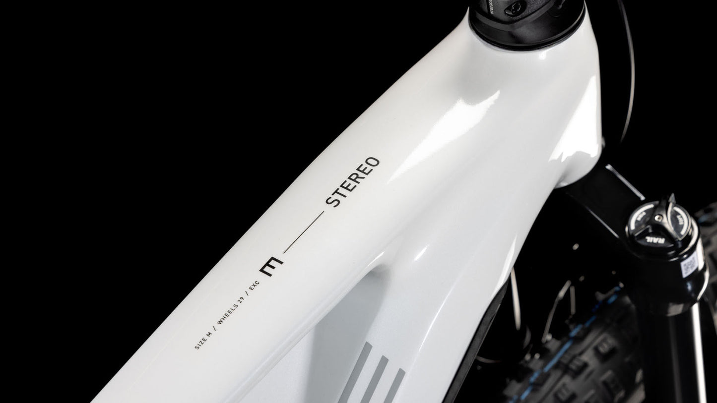Die Nahaufnahme des CUBE Stereo Hybrid ONE44 EXC 800 in Weiß-Schwarz-Metallic (2025) zeigt den modernen Rahmen mit "STEREO"-Schriftzug, Shimano XT-Komponenten und eine sichtbare Federgabel.