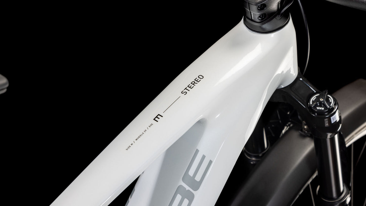 Nahaufnahme des Oberrohrs des CUBE Stereo Hybrid ONE44 EXC 800 Allroad metallicwhite'n'black 2025 Rahmens mit dem Schriftzug "STEREO" und einer teilweise gefederten Vorderradgabel vor schwarzem Hintergrund.