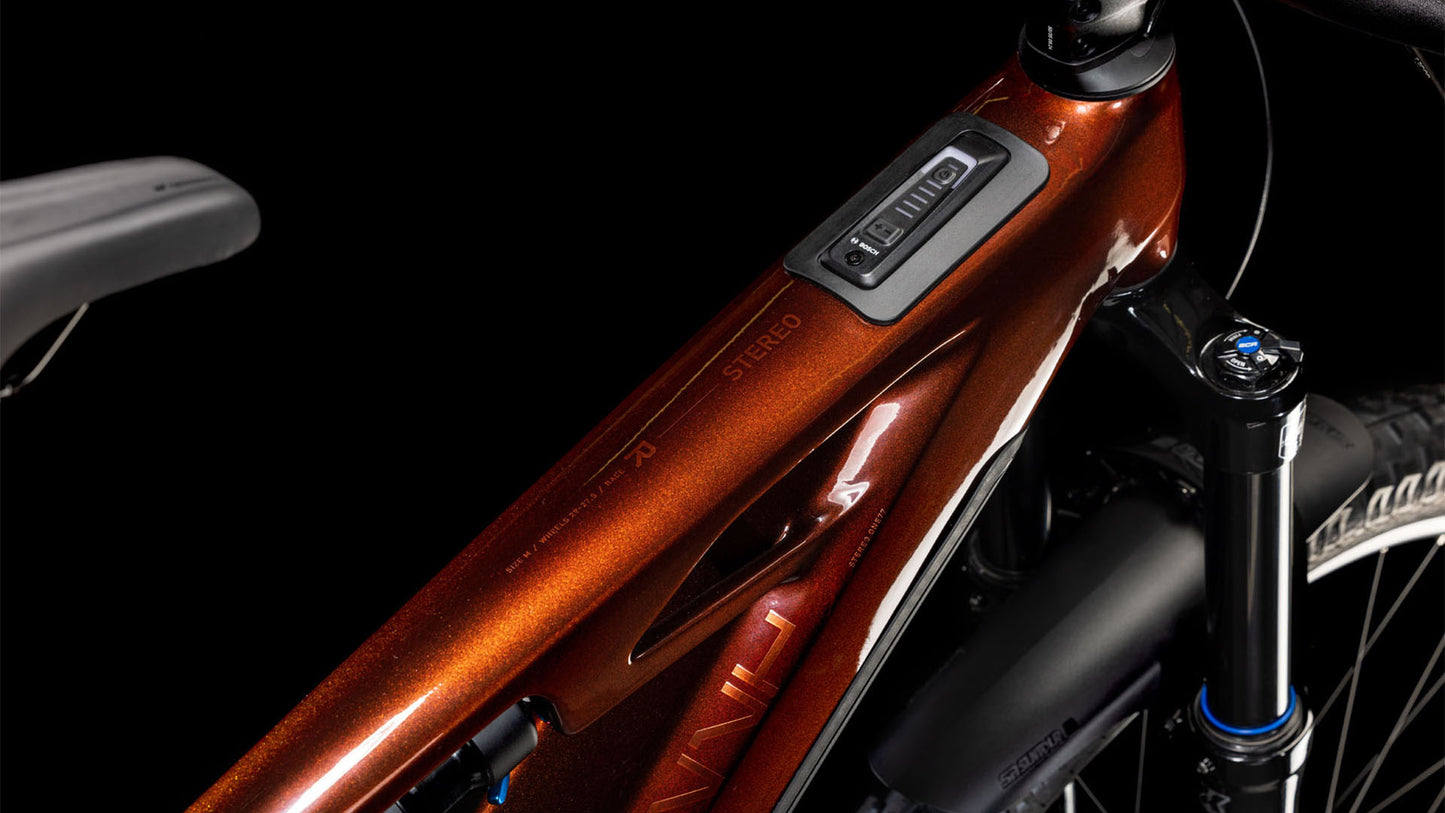 Nahaufnahme des CUBE Stereo Hybrid ONE77 HPC Race 800 liquidorange'n'orange 2025 Rahmens mit Fokus auf das Oberrohr mit integriertem Display; das glänzende Finish und die modernen Designdetails heben sich von einem schwarzen Hintergrund ab.