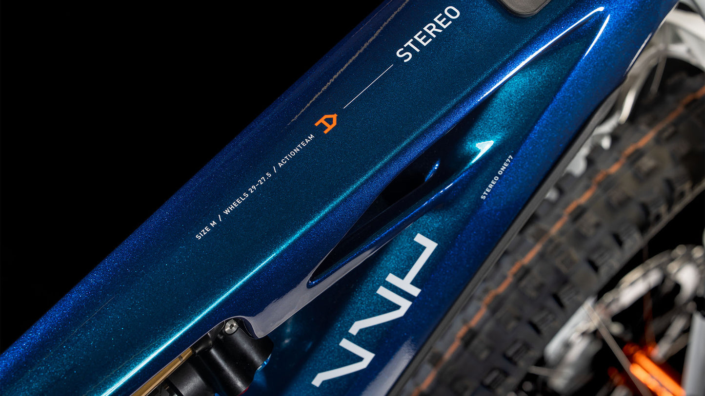 Nahaufnahme des blauen CUBE Stereo Hybrid ONE77 HPC AT 800 Actionteam 2025-Rahmens mit technischen Details und STEREO-Branding in der Nähe des Hinterreifens, wobei ein Teil der Federung und die Shimano XT-Scheibenbremsen sichtbar sind.