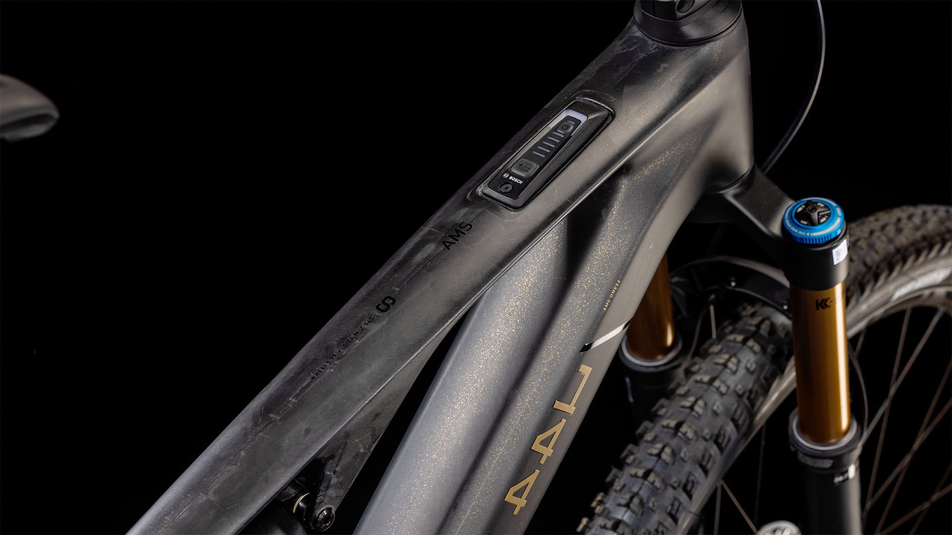 Nahaufnahme des CUBE Cube AMS Hybrid ONE44 C:68X SLT 400X 29 carbon'n'golddust 2025, ein mattschwarz-goldenes vollgefedertes Mountainbike mit Bosch SX-Antrieb, Bedienfeld am Oberrohr und C:68X-Carbonrahmen vor schwarzem Hintergrund.