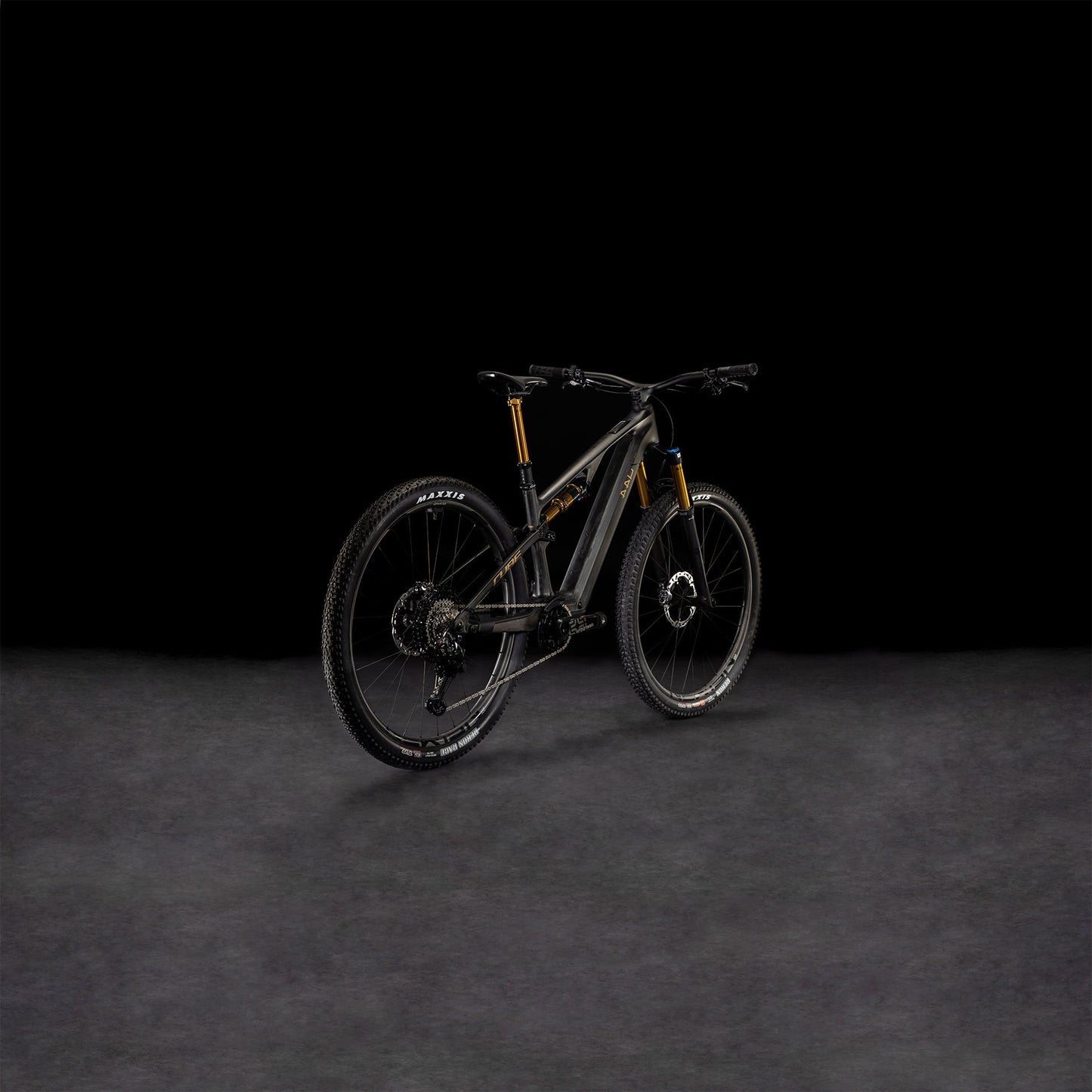 Das CUBE AMS Hybrid ONE44 C:68X SLT 400X 29 carbon'n'golddust 2025, ein schwarzes, vollgefedertes MTB mit goldenen Akzenten und einem C:68X-Carbonrahmen, ist von hinten auf einer dunklen, strukturierten Oberfläche vor einem schwarzen Hintergrund abgebildet.