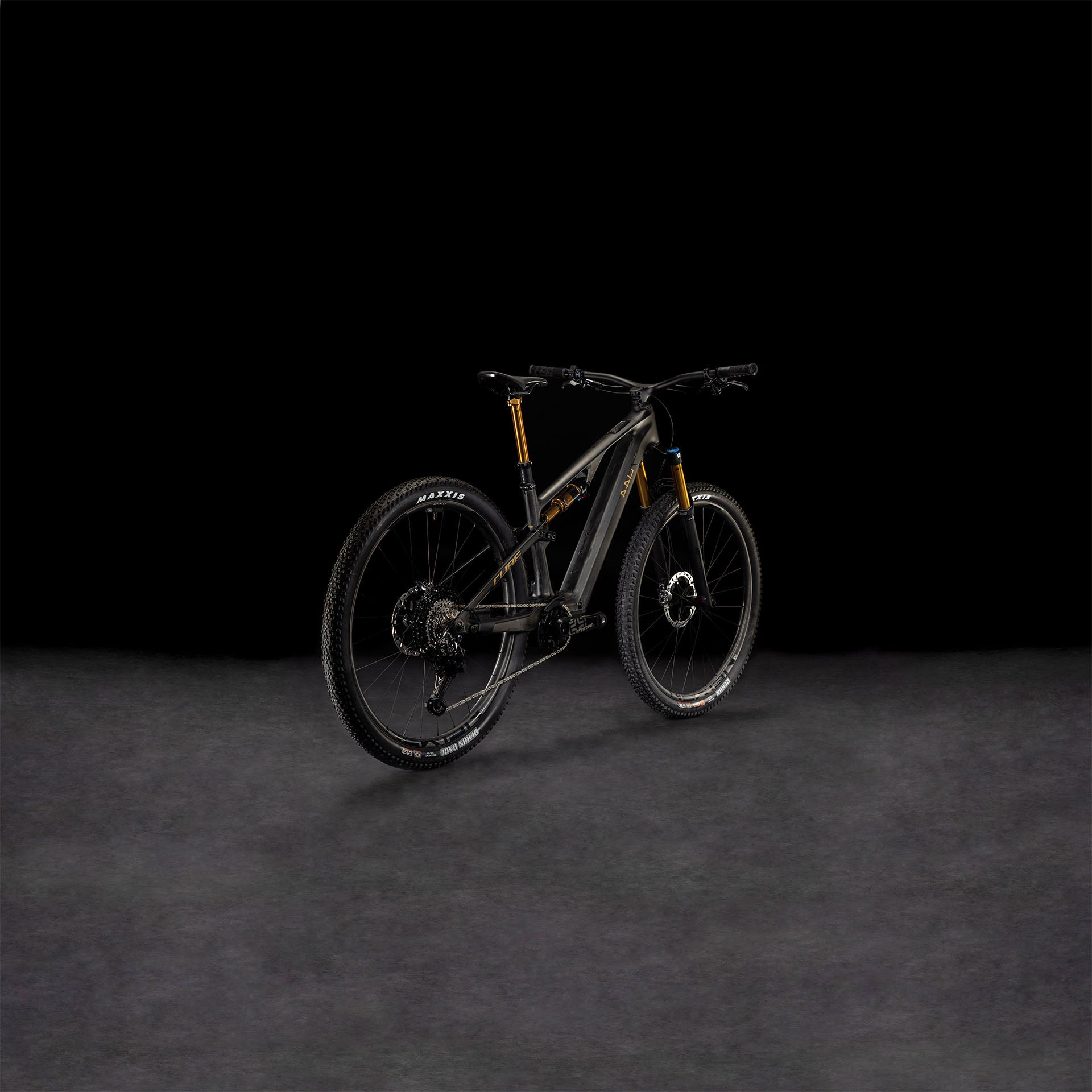 Das CUBE AMS Hybrid ONE44 C:68X SLT 400X 29 carbon'n'golddust 2025, ein schwarzes, vollgefedertes MTB mit goldenen Akzenten und einem C:68X-Carbonrahmen, ist von hinten auf einer dunklen, strukturierten Oberfläche vor einem schwarzen Hintergrund abgebildet.