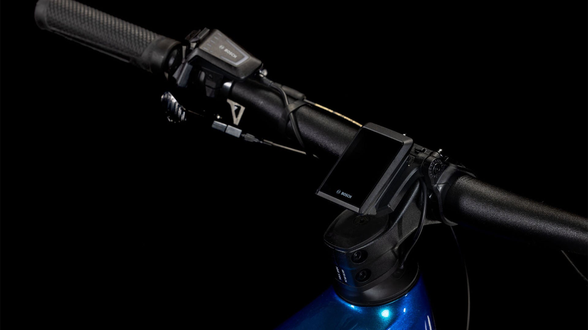 Nahaufnahme des CUBE Reaction Hybrid SLX 800 nebula'n'blue 2025 Lenkers mit montiertem Digitaldisplay und Bedientasten, wobei ein Teil des metallisch blauen Rahmens vor schwarzem Hintergrund sichtbar ist.