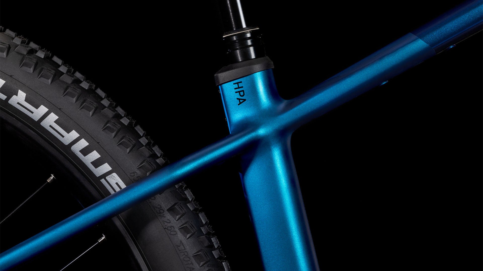 Nahaufnahme des CUBE Reaction Hybrid SLX 800 nebula'n'blue 2025 Rahmens, die den Sattelrohrübergang, die Sattelstütze und einen Teil des knorrigen Hinterreifens auf schwarzem Hintergrund zeigt. Der Schriftzug "HPA" ist auf dem Rahmen sichtbar.