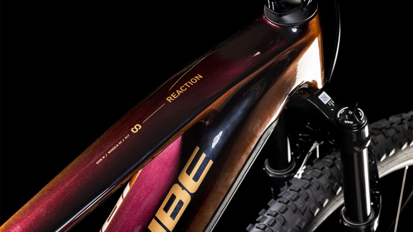 Nahaufnahme des Cube Reaction Hybrid SLT 800 solareclipse'n'bronze 2025 Rahmens, die das Oberrohr mit CUBE-Branding und ein glänzendes dunkelrot-braunes Gradientenfinish zeigt. Sichtbar: ein Teil des Vorderrads, der Gabel und des integrierten PowerTube-Akkus.