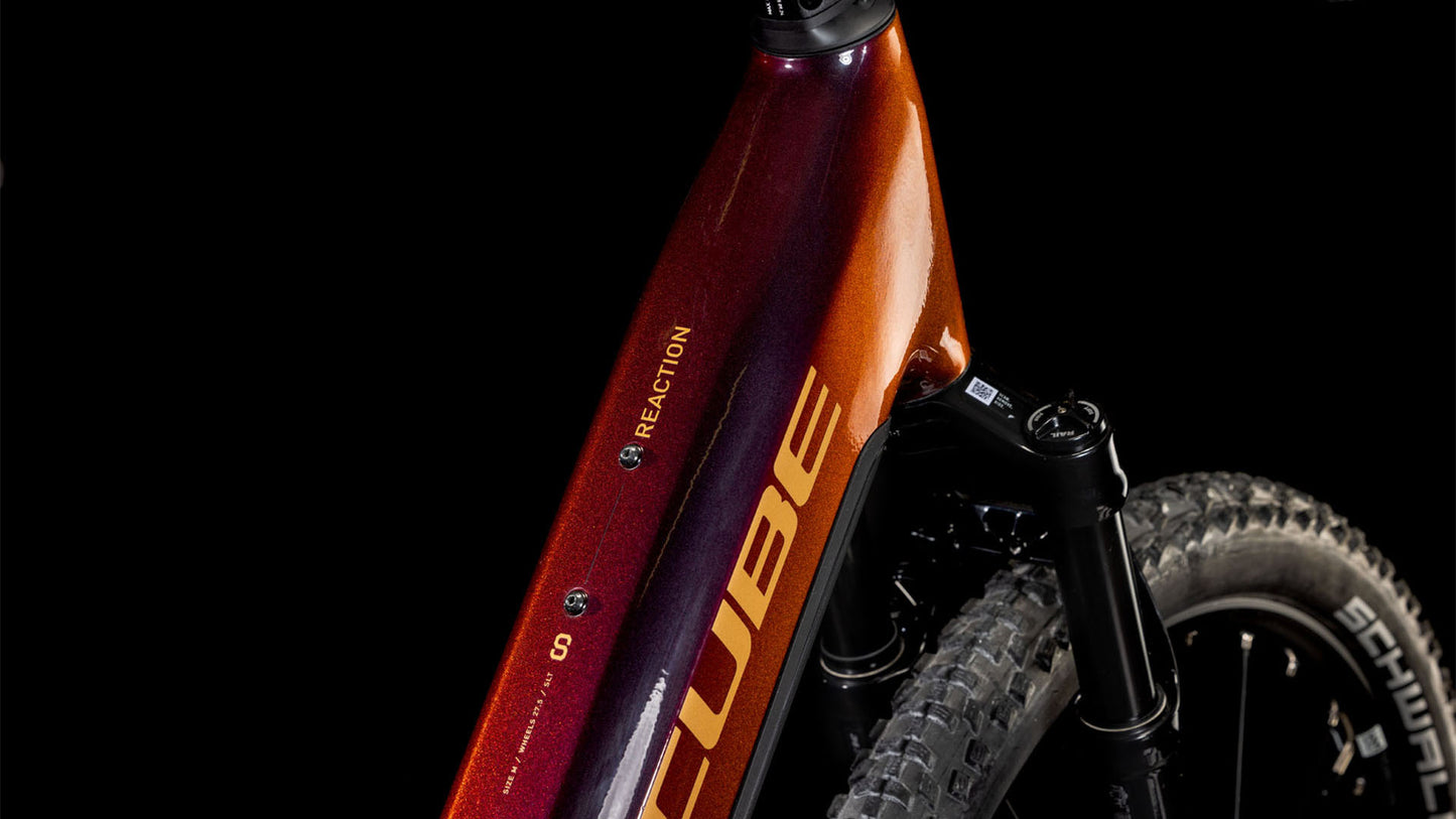 Nahaufnahme eines CUBE Reaction Hybrid SLT 800 solareclipse'n'bronze Easy Entry 2025-Rahmens mit orange-bronzefarbenem Farbverlauf. Zu sehen sind das CUBE-Logo, das REACTION-Label, die Federgabel, der PowerTube-Akku und ein Teil des Vorderradreifens vor einem schwarzen Hintergrund.