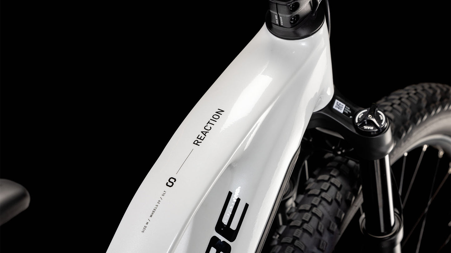 Nahaufnahme eines CUBE Reaction Hybrid SLT 800 metallicwhite'n'black Trapeze 2025 Rahmens, die das Oberrohr mit REACTION Branding und einen Teil der Federgabel und des Reifens vor schwarzem Hintergrund zeigt.