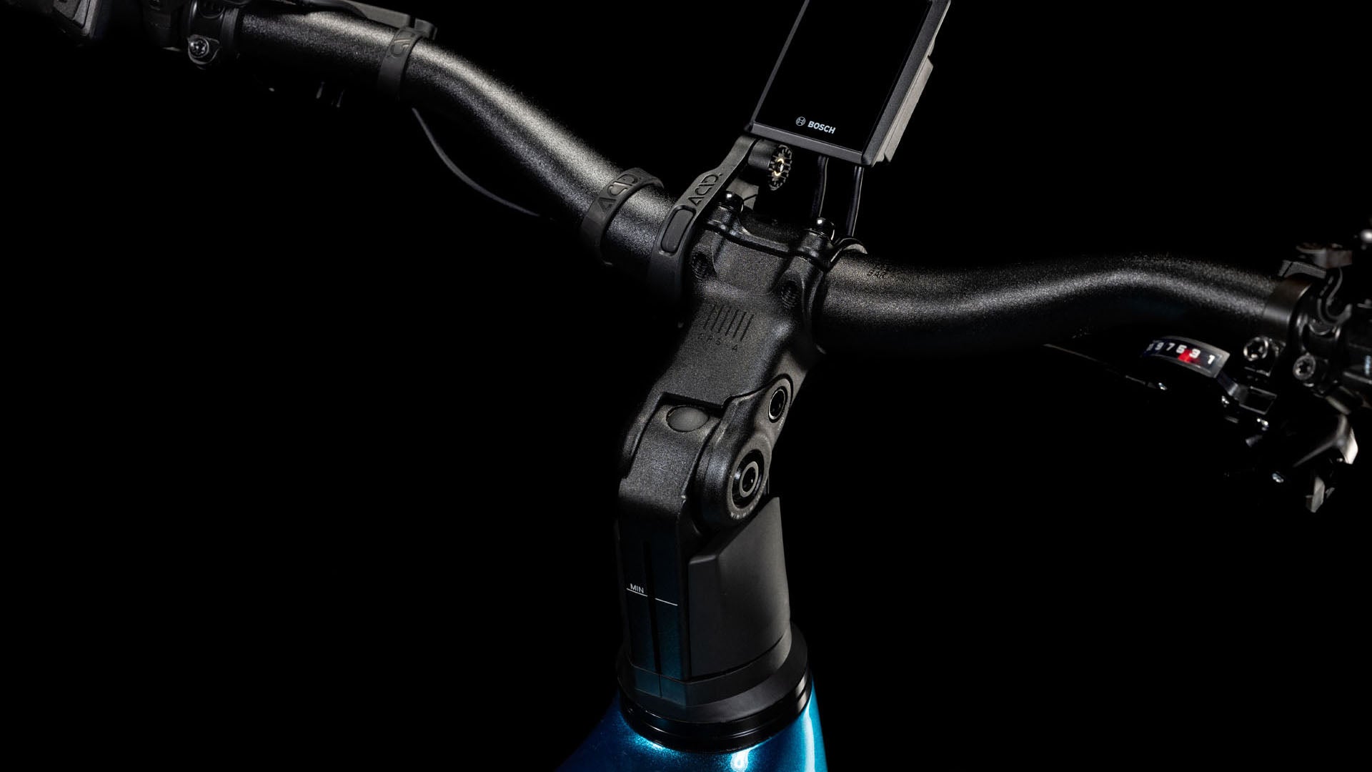 Nahaufnahme eines CUBE Kathmandu Hybrid EX 800 electricblue´n´chrome 2025-Lenkers mit montierter Digitalanzeige, Gangschaltung und Teil des Rahmens vor einem schwarzen Hintergrund.