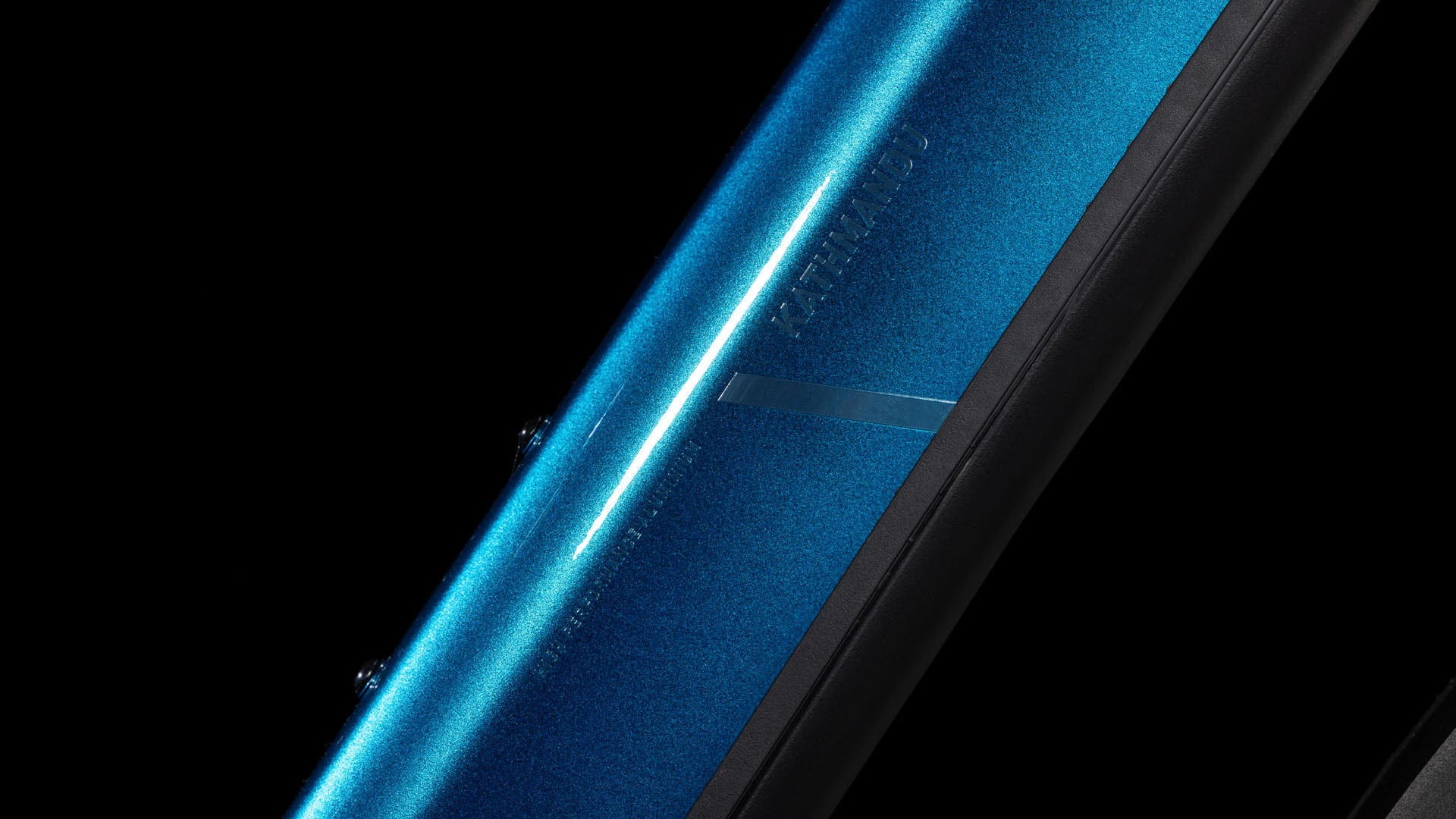 Nahaufnahme eines CUBE Kathmandu Hybrid EX 800 electricblue´n´chrome 2025 Rahmenrohrs mit glänzendem Metallic-Blau-Finish vor schwarzem Hintergrund. Dezentes Branding und Bolzenaufnahmen sind auf der Oberfläche sichtbar.