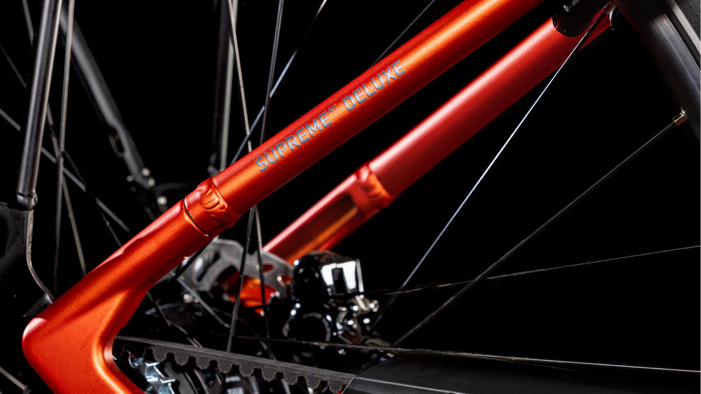 Nahaufnahme des CUBE Supreme RT Hybrid Deluxe EX 625 in Fireorange & Lunar mit Rahmen, Kette, Gängen und Speichen vor schwarzem Hintergrund – ein elegantes Beispiel für die Präzision des CUBE E-Bikes mit einfachem Einstieg aus dem Jahr 2025.