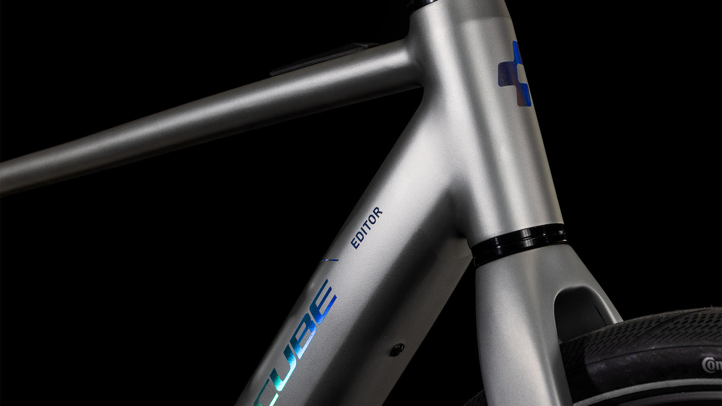 Nahaufnahme des CUBE Editor Hybrid SLX 400X sleekgrey'n'spectral 2025 mit blauem CUBE-Schriftzug, modernem silbernen Rahmen, Shimano 8-Gang-Nabenschaltung und einem Teil des Vorderrads vor schwarzem Hintergrund.
