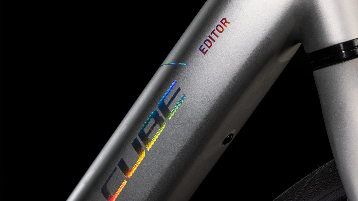 Nahaufnahme des CUBE Editor Hybrid SLX 400X sleekgrey'n'spectral 2025-Rahmens mit holografischem "CUBE"- und rotem "EDITOR"-Schriftzug, mit Bosch SX E-Motor, vor schwarzem Hintergrund.