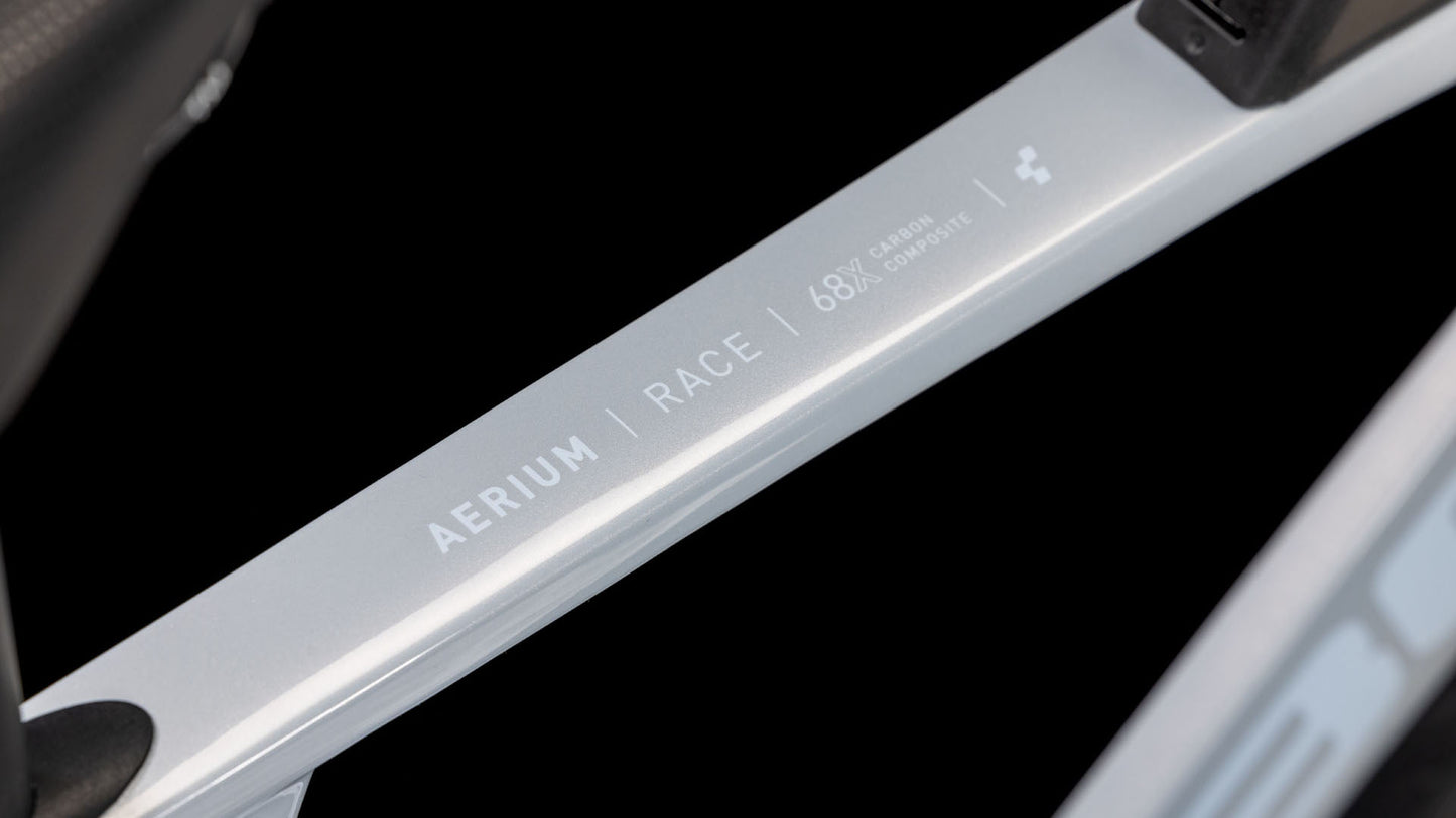 Nahaufnahme eines CUBE Aerium C:68X Race foggrey'n'white 2025 Rahmens mit der Aufschrift "C:68X | RACE | 68% CARBON COMPOSITE" auf der Metalloberfläche vor schwarzem Hintergrund.