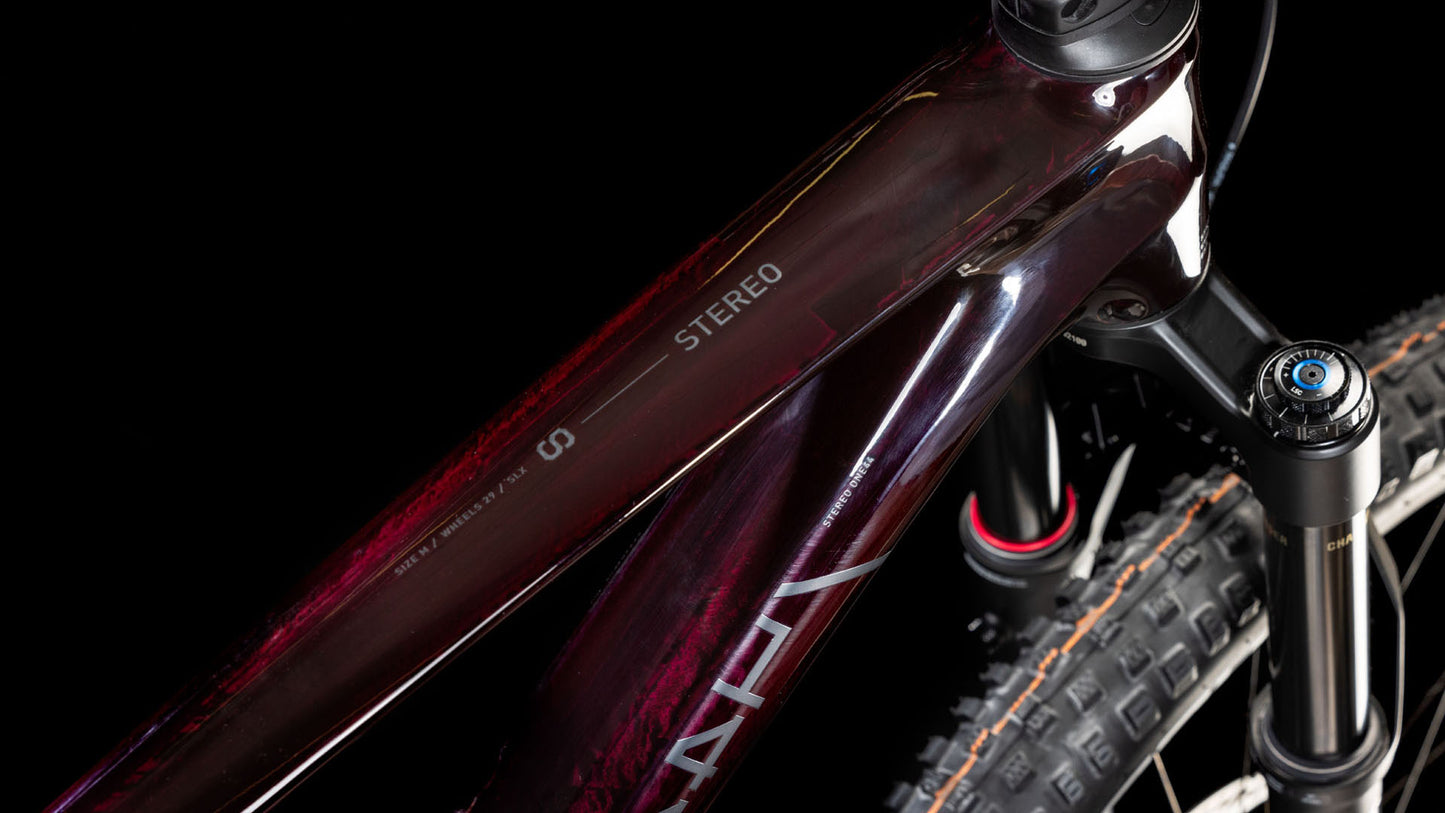 Nahaufnahme des Oberrohrs und der Vorderrad-Federgabel eines CUBE Stereo ONE44 C:68X SLX 29 liquidviolet'n'black 2025 Mountainbikes. Zu sehen sind das STEREO-Label, das sichtbare Reifenprofil und Rahmendetails vor einem schwarzen Hintergrund.