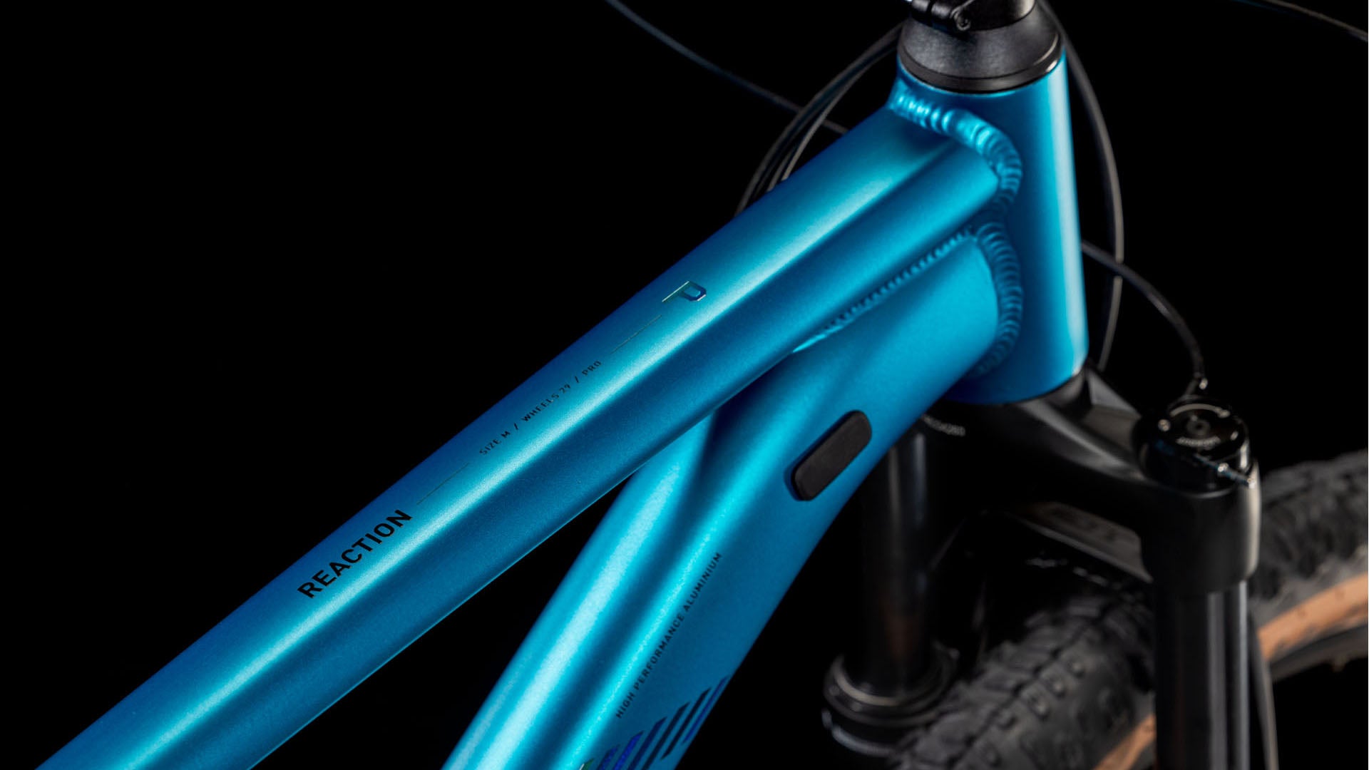 Nahaufnahme des CUBE Reaction Pro metallicteal'n'holo 2025 Rahmens mit REACTION auf dem Oberrohr, detaillierten Schweißnähten, RockShox Judy Silver Luftfedergabel und Federgabel vor einem schwarzen Hintergrund.
