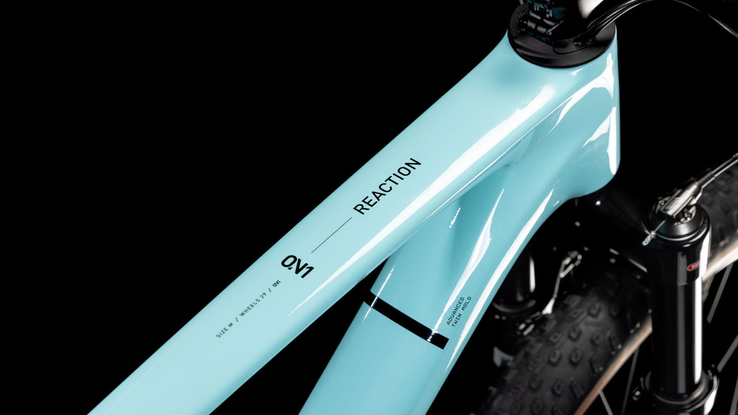 Nahaufnahme des CUBE Reaction C:62 ONE dazzle'n'black 2025 Rahmens mit REACTION und QVI auf dem Oberrohr, mit einer Teilansicht der schwarzen Federgabel und des Reifens vor einem schwarzen Hintergrund.