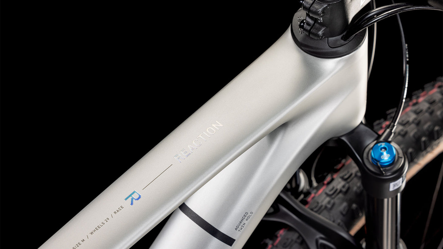 Nahaufnahme eines CUBE Reaction C:62 Race sleek grey'n'prism 2025 Rahmens mit "REACTION" Schriftzug, mattem Metallic-Finish und einem Teil der vorderen Federgabel, die sich schwarz abhebt. Mit Shimano XT Schaltung.