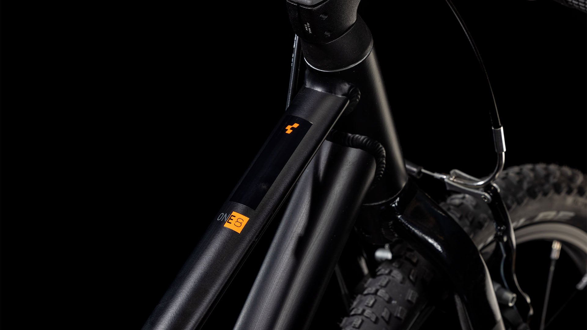 Nahaufnahme des Vorderrahmens und des Laufrads des CUBE Numove 180 black'n'orange 2025 mit schlankem Design, Schwalbe-Reifen, einem kleinen orangefarbenen Logo und Etikett auf dem 6061-Aluminiumrahmen vor einem dunklen Hintergrund.