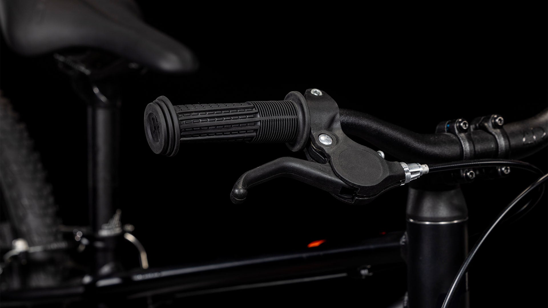 Nahaufnahme des Cube Numove 180 black'n'orange 2025 von CUBE - mit schwarzem Lenker mit strukturiertem Gummigriff, Bremshebel und einem Teil des 6061er-Aluminiumrahmens und -sitzes, perfekt für jeden All-Terrain-Bike-Enthusiasten.