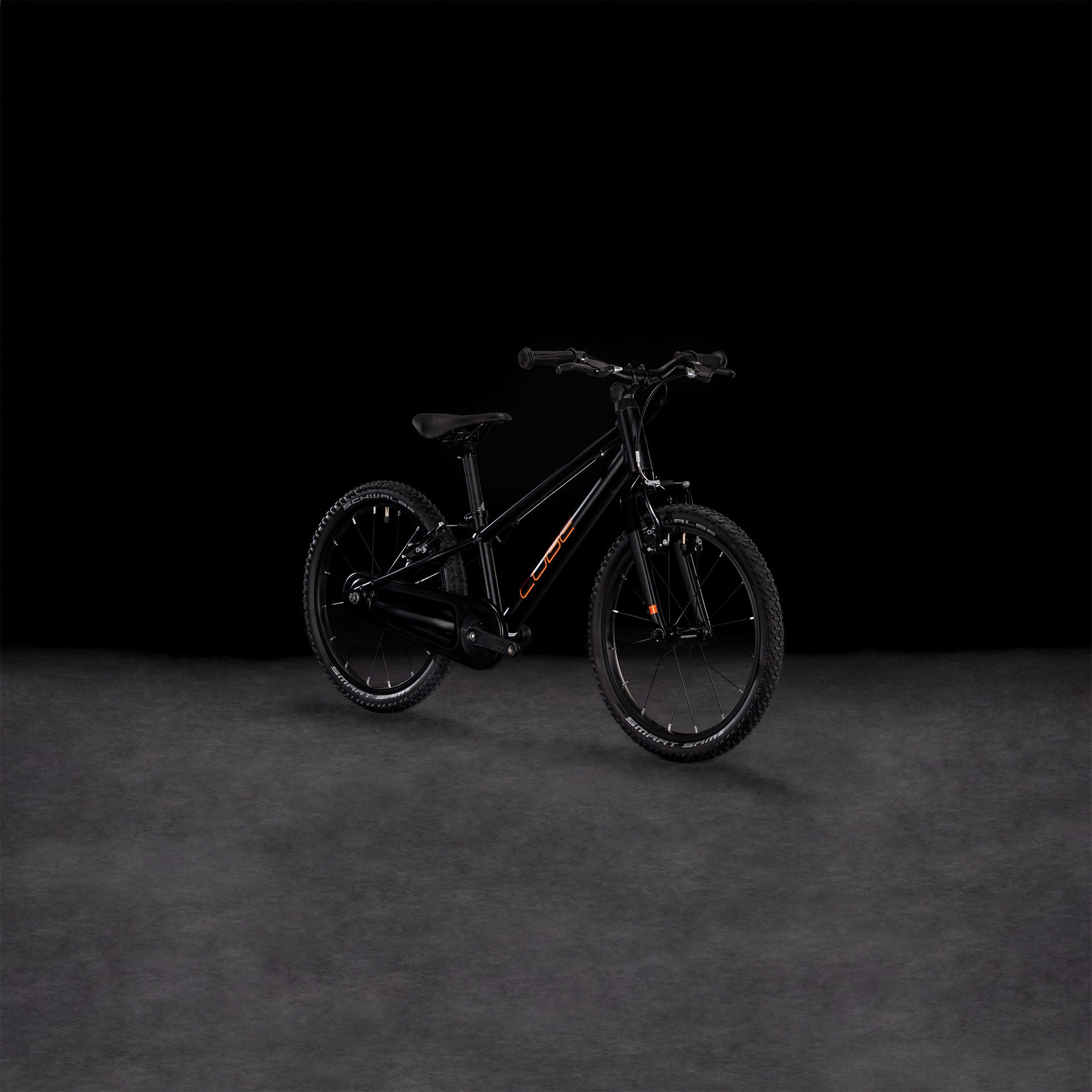 Das CUBE Numove 180 black'n'orange 2025, ein Kinder-Geländefahrrad aus robustem 6061er-Aluminium, zeigt sich im Seitenprofil vor einem dunklen Hintergrund. Der schwarze Rahmen ist mit auffälligen orangefarbenen Akzenten versehen.