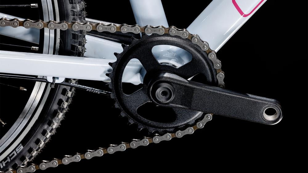 Nahaufnahme der Kurbelgarnitur, des Kettenblatts und der Kette des CUBE Numove 200 flashwhite'n'pink 2025 mit sichtbarem Hinterreifen. Der leichte CUBE-Rahmen hebt sich vom schwarzen Hintergrund ab und verfügt über eine 8-Gang-Schaltung für reibungslose Schaltvorgänge.