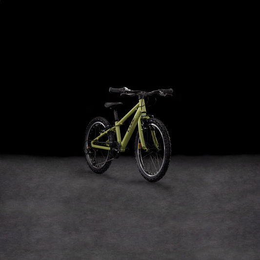 Ein CUBE Acid 200 lightolive'n'orange 2025 Kinder-Mountainbike mit schwarzen Rädern, Lenker und V-Bremsen steht auf einer dunkel strukturierten Oberfläche vor einem schwarzen Hintergrund.