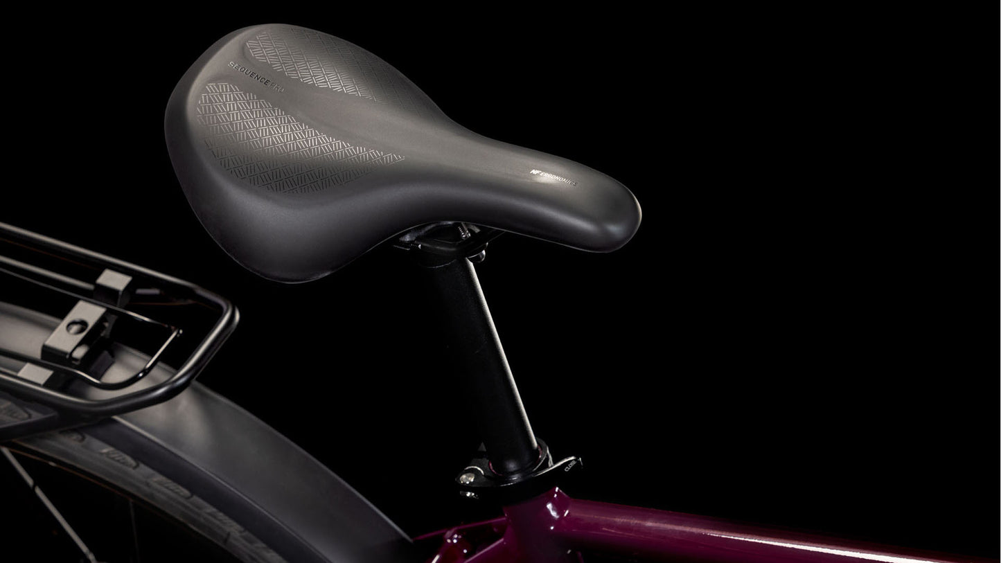 Nahaufnahme eines schwarzen Fahrradsattels und einer Sattelstütze auf einem dunkelvioletten CUBE Nature ONE Allroad amarone'n'lunar 2025 Rahmen, wobei ein Teil des Hinterrads und des Gepäckträgers vor einem schwarzen Hintergrund sichtbar ist.