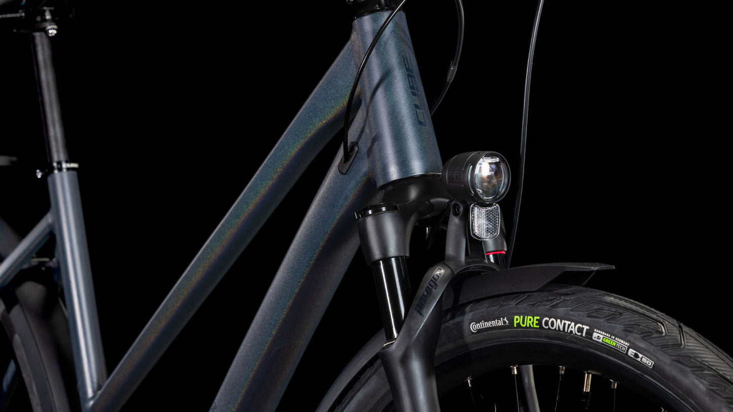 Nahaufnahme des Cube Kathmandu SLX nightsky'n'ink Trapeze 2025 von CUBE, die den Rahmen, den Scheinwerfer, die Federgabel, den Continental PureContact-Reifen und das Shimano Cues 2x11-Gang Schaltungsset vor einem schwarzen Hintergrund zeigt.