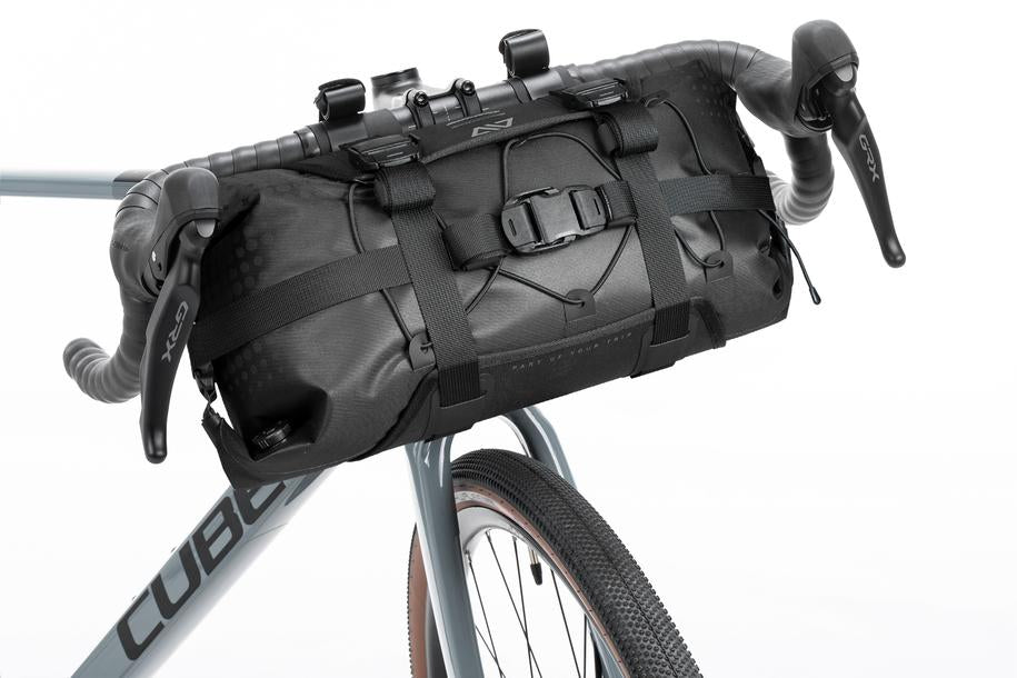 Eine Nahaufnahme der schwarzen ACID Lenkertasche PACK PRO 15 von ACID, sicher befestigt an einem grauen Fahrrad - ideal für Bikepacking. Erhältlich im CUBE Store in Hildesheim, Niedersachsen.
