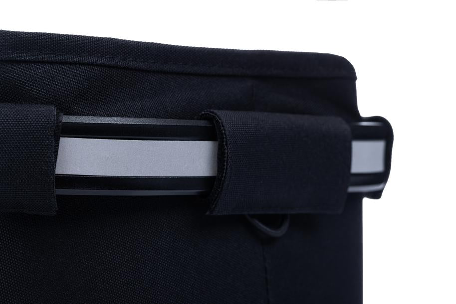Nahaufnahme des ACID Gepäckträgerkorbs CITY 20 RILink black von ACID mit einem silber-schwarzen Griff, der teilweise von einer Stoffschlaufe bedeckt ist, auf weißem Hintergrund. Subtile reflektierende Elemente erhöhen sowohl den Stil als auch die Sicherheit.