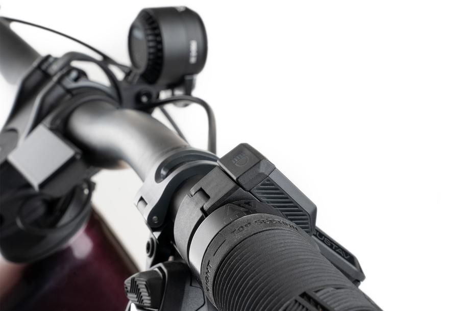 Nahaufnahme eines Fahrradlenkers mit strukturiertem Gummigriff, ACID E-Bike Frontlicht PRO-E 200 High Beam X-Connect schwarz mit StVZO-Zertifizierung und Steuerschalter von ACID vor weißem Hintergrund.