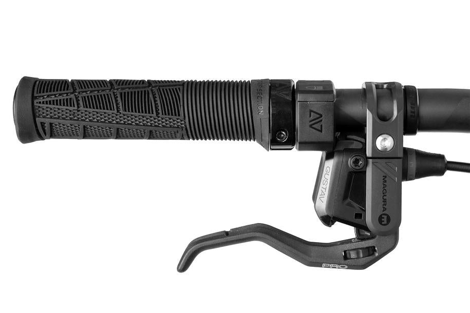 Nahaufnahme eines schwarzen Fahrradlenkers mit strukturiertem Griff, Gangschaltung, hydraulischem MAGURA-Bremshebel und dem ACID E-Bike Frontlicht PRO-E 200 High Beam X-Connect (StVZO-zertifiziert) mit detaillierten Komponenten und Kabelverbindungen.