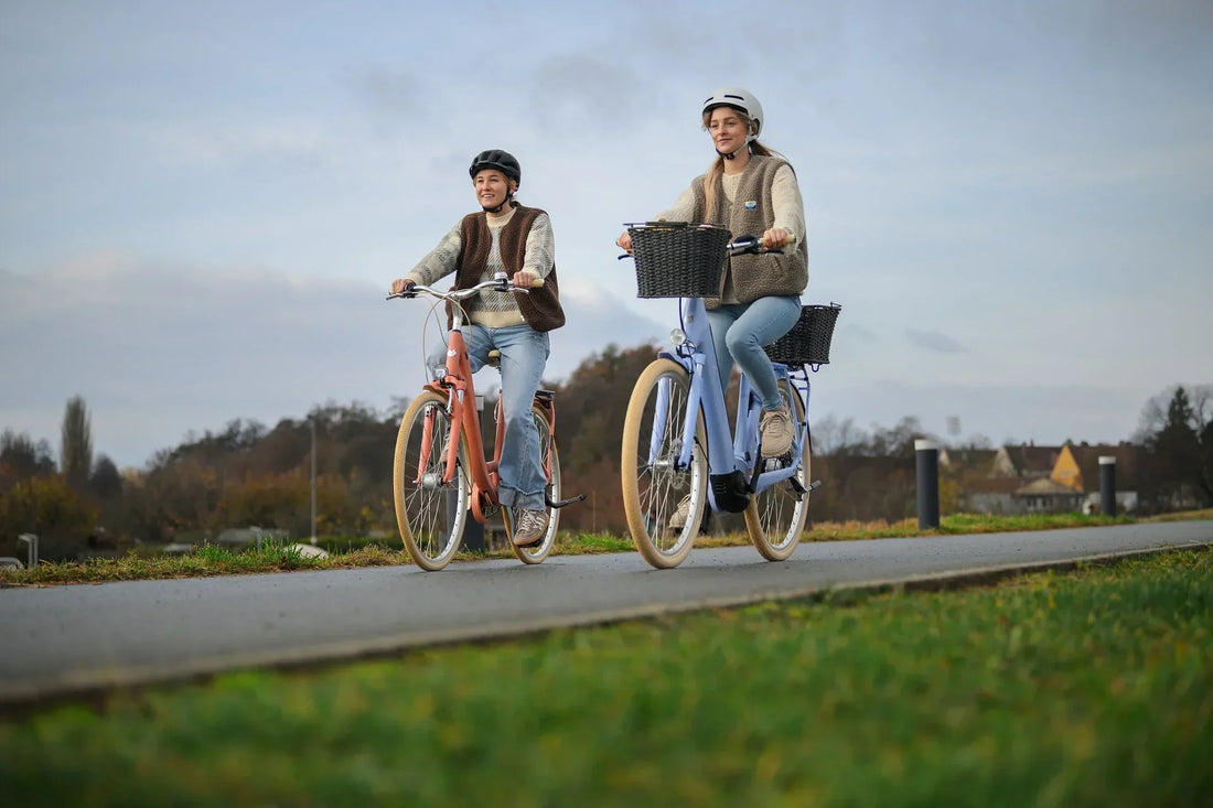 Zwei Personen fahren auf CUBE City-E-Bikes in Rot und Hellblau über einen Radweg im Grünen