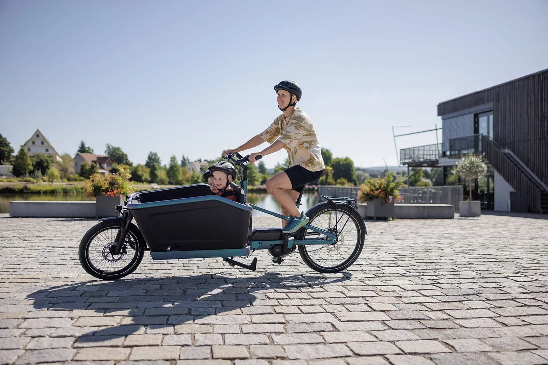 Person fährt ein CUBE Cargo Lastenrad mit Kind in der Transportbox vor modernen Gebäuden