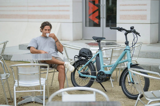 Mann trinkt Kaffee in einem Café, daneben ein türkises CUBE Compact Kompakt-E-Bike mit kleinen Laufrädern
