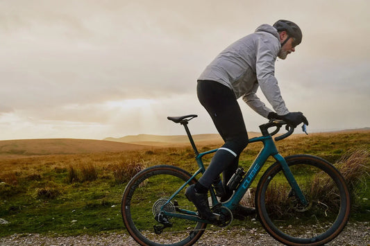 Radfahrer fährt auf einem CUBE Gravelbike einen Schotterweg in hügeliger Landschaft im Abendlicht