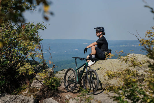 Mountainbiker macht Pause auf einem Felsen mit Panoramablick, daneben ein CUBE Hardtail-Mountainbike