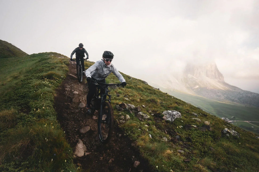 Zwei Mountainbiker fahren auf CUBE E-MTBs einen schmalen Bergpfad in neblige Berge hinauf