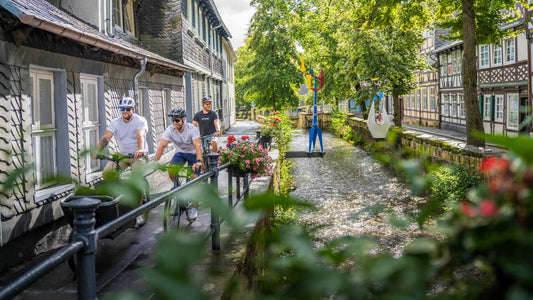 Drei Radfahrer fahren entlang eines Bachlaufs zwischen Fachwerkhäusern in einer Altstadt